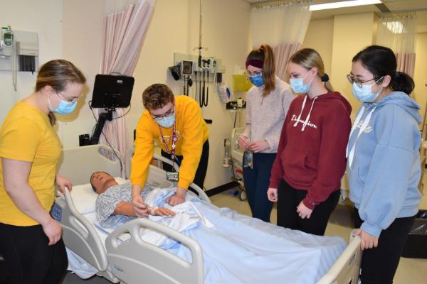 Group of students standing around a mannequin watch a skills demonstration